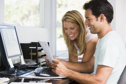A man and a woman examine a document while working together on a desktop computer